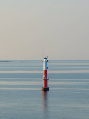 Güneşli bir günde mavi denizde duran bir deniz fenerinin dikey görüntüsü.