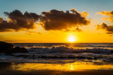 Bulutlu bir gün batımını yansıtan kumlu bir sahilin güzel bir görüntüsü.