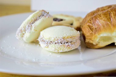 Beyaz bir tabakta alfajor, kruvasan ve diğer hamur işlerinden oluşan bir kahvaltının yakın çekimi.