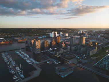 Bulutlu bir gökyüzü ve ufukta gün batımı olan bir şehir manzarası.