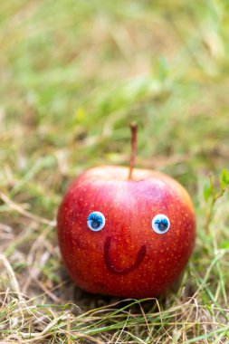 Kırmızı bir elmanın dikey görüntüsü, şaşı gözleri ve gülüşü.