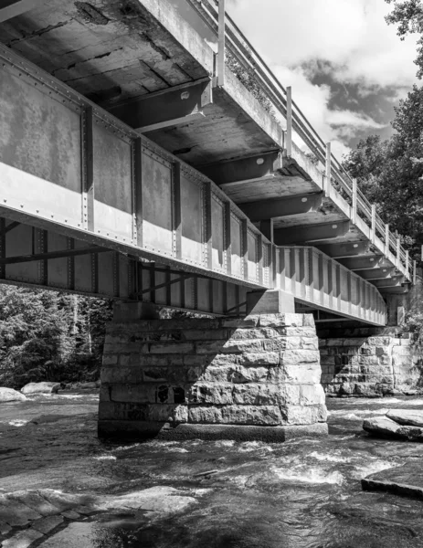 Pionowe Czarno Białe Ujęcie Mostu Nad Rzeką Zachmurzonym Tle Nieba — Zdjęcie stockowe