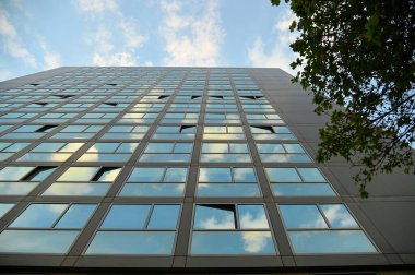 Modern bir binanın camının alçak açılı görüntüsü bulutlu gökyüzünü yansıtıyor.