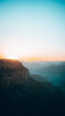 Parlak güneş mavi ve turuncu günbatımı gökyüzünde bir kayanın üzerinde parlıyor.