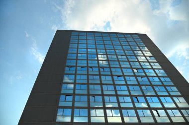 Modern bir binanın camının alçak açılı görüntüsü bulutlu gökyüzünü yansıtıyor.