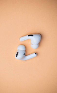 Beyaz kablosuz kulaklıkların dikey görüntüsü turuncu arka planda izole edilmiş.