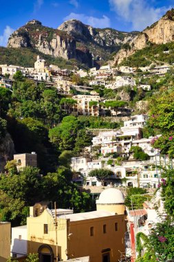 Positano, İtalya 'da yeşilliklerle çevrili bir dağdaki köy evlerinin dikey görüntüsü.