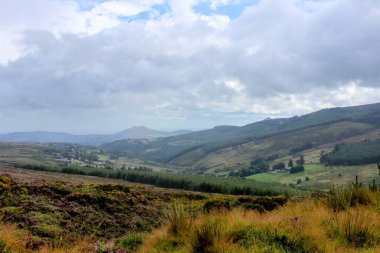 Bulutlu gökyüzünün altında tarlaları ve tepeleri olan güzel bir manzara.