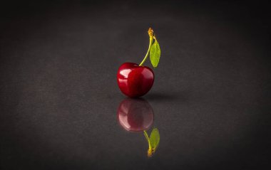 Yansıtıcı gri bir yüzey üzerinde yaprağı olan sulu kırmızı bir kiraz.