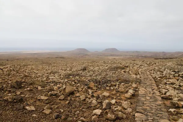 一条石路穿过岩石的露头 地平线上有一座小山 — 图库照片