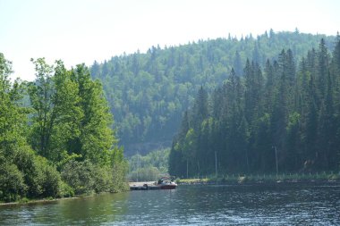 Bir gölün kıyısında, yoğun dağ ormanları ve yeşil dağların arasında rıhtıma yanaşmış bir tekne.