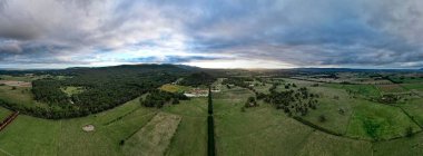 Gün batımında, bulutlu bir günde yeşil tarlalar ve ağaçlarla çevrili bir üzüm bağının panoramik görüntüsü.