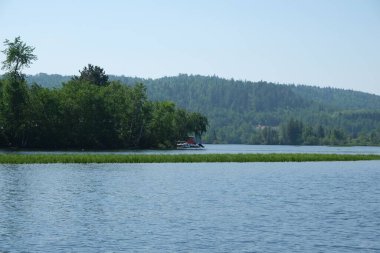 Göl kıyısında, sık ormanların arasında rıhtıma yanaşmış bir tekne.