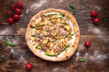 Tahta bir masada sebzeli ve kiraz domatesli lezzetli ve çıtır çıtır bir pizzanın üst görüntüsü.