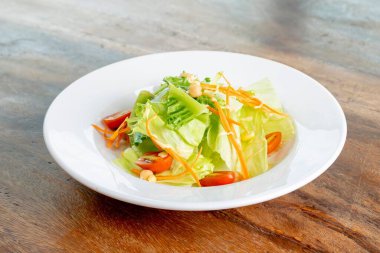 Beyaz bir tabakta servis edilen domatesli, marullu ve havuçlu bir salata.