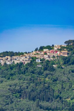 Gaios köyünde bulutsuz bir günde ağaçlarla çevrili dağdaki evlerin dikey görüntüsü.