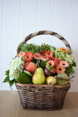 Güzel bir çiçek buketinin dikey görüntüsü. Tahta bir masanın üzerindeki sepetin içindeki meyveler.