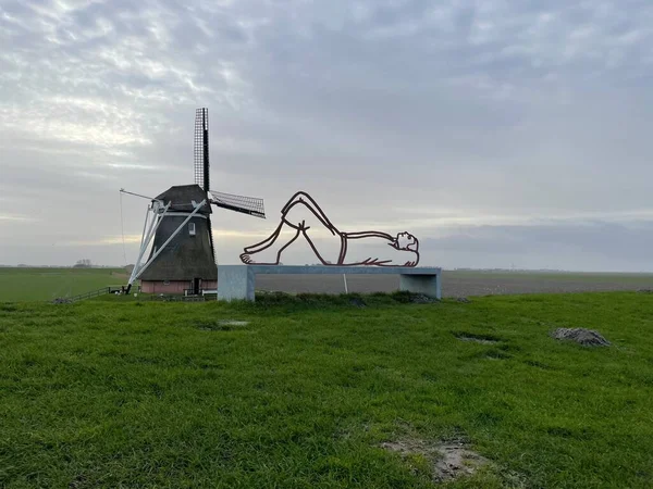 Een Man Standbeeld Liggend Naast Molen Met Groen Gras Rond — Stockfoto