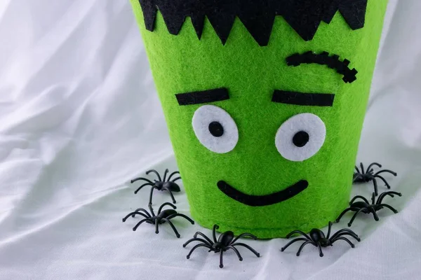 A Halloween Green monster candy bag in a nest of black plastic spiders