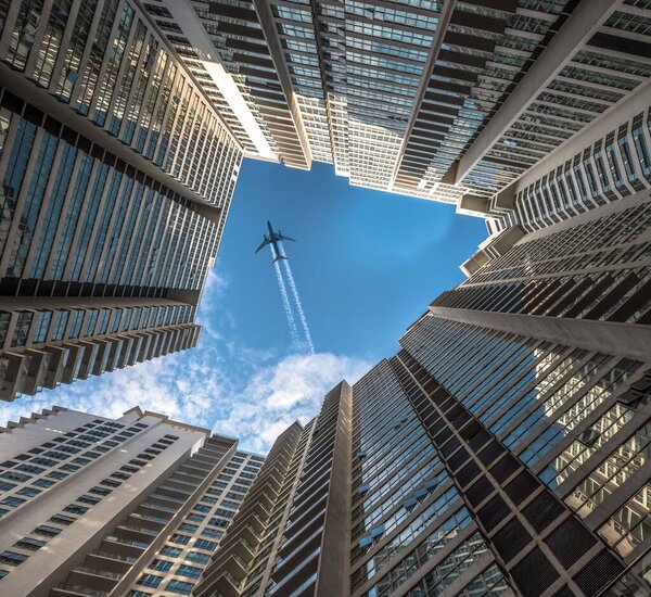 A bottom view from the buildings of a plane in the blue sky
