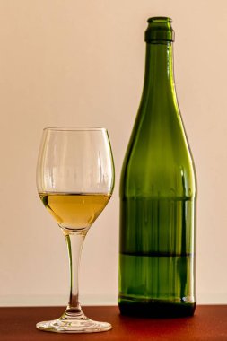 Masada yeşil şarap şişesi olan beyaz bir bardağın dikey görüntüsü.