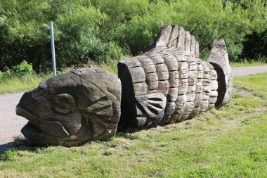 Büyük balığın ahşap heykelinin yakın çekimi. Arka planda ağaçlar olan bir yol kenarında.