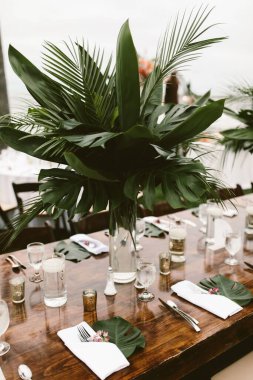 Bir açık hava etkinliğinde yeşil tropikal çiçekli bir masanın dikey görüntüsü.