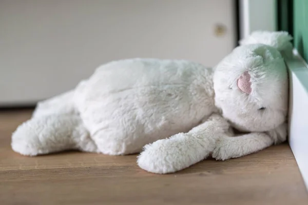 A white stuffed toy lying on a wooden floor