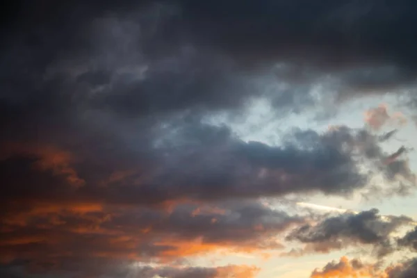 オレンジ色の夕日に照らされた空の曇り空の灰色の雲の美しいショット — ストック写真