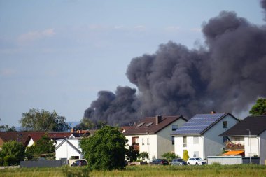 Gökyüzüne yükselen siyah dumanlı araçları olan evler.