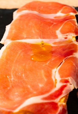 Kırmızı Serrano jambonu siyah bir yüzey üzerinde dilimler.