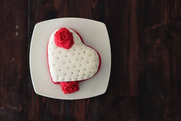 A top view of a plate with a romantic heart-shaped pastry with marizpan red roses