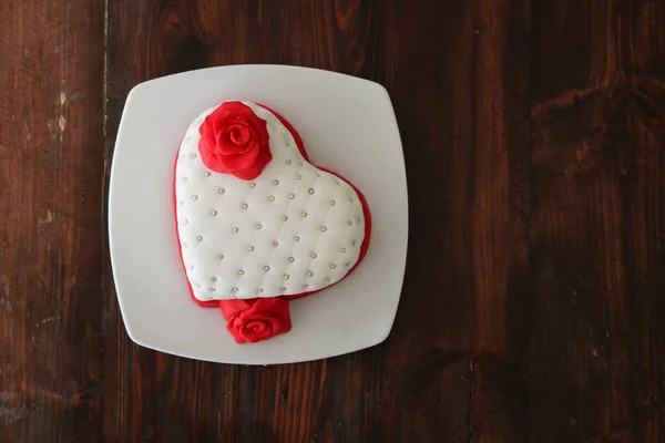 A top view of a plate with a romantic heart-shaped pastry with marizpan red roses