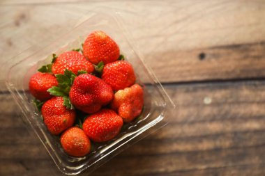 Tahta bir masada plastik bir tabakta kırmızı sulu çileklerin üst görüntüsü.