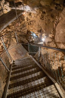 Bir mağaraya giden metalik merdivenlerin dikey görüntüsü.