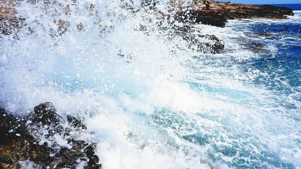 天气晴朗时 蓝色海浪拍到岩石海岸的特写 — 图库照片