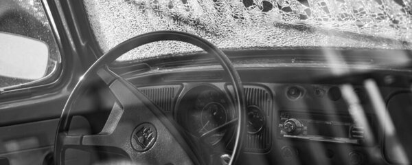 A panoramic black and white shot of the interior of an old classic car with broken windshield