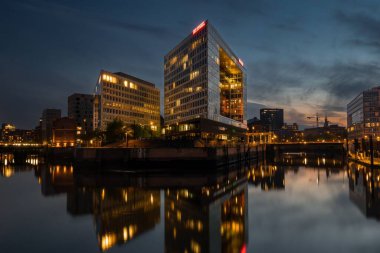 Mavi saatte Hamburg 'daki Spiegel binasında Elbe nehrinde yansımalar var. gün batımı arkaplanda.
