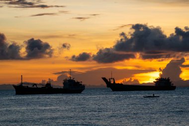 Deniz kenarında bir gün doğumu, iki gemi ve küçük bir tekne silueti.