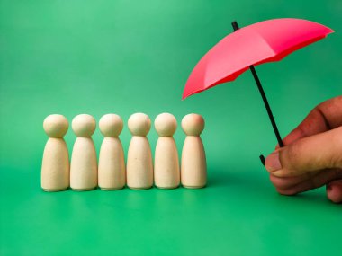 El ele tutuşan kırmızı şemsiye ve yeşil arka planda izole edilmiş tahta bebekler.