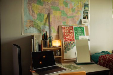 Yatak odasında masa, dizüstü bilgisayar ve malzemelerle rahat bir çalışma köşesi.