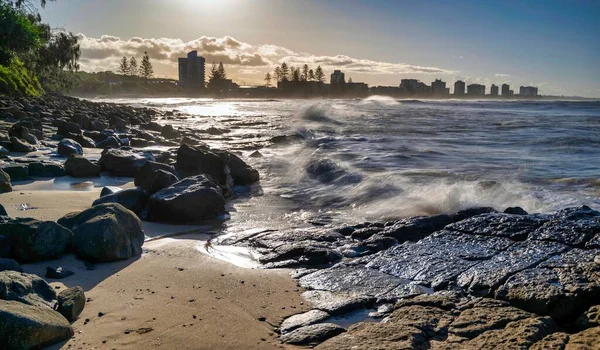 在城市景观的背景下 一个被柔和的海浪拍打着的浸透阳光的岩石海滩 — 图库照片