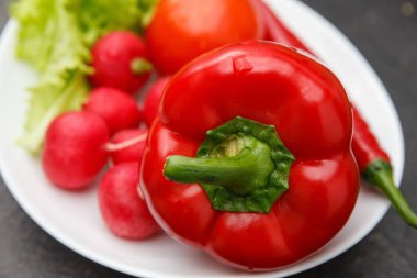 Taze sebze, kırmızı biber, acı biber, turp, domates ve yeşil salatayı koyu ahşap yüzeyde beyaz tabakta yakın plan çek.