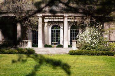 Bitkilerle çevrili büyük sütunları olan bir Viktorya dönemi binası.