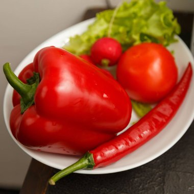 Taze sebze, kırmızı biber, acı biber, turp, domates ve yeşil salatayı koyu ahşap yüzeyde beyaz tabakta yakın plan çek.