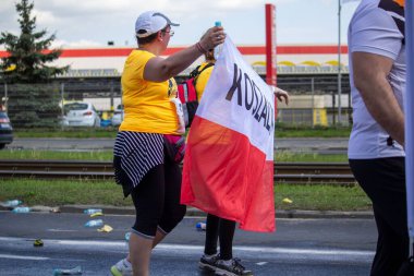 Bir grup sarı gömlekli insan, Wings for Life World Run 'da Polonya bayrağı taşıyor.