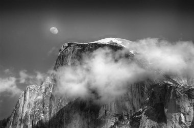 Arka planda ay olan, tepeyi kaplayan bir bulutun gri pulu