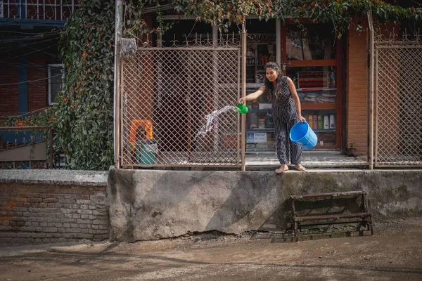 Женщина Брызгает Водой Улицу Перед Своим Домом Пыли Машина Проходит — стоковое фото