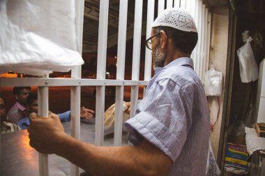 Bahreyn şehrinde bir adam parmaklıklı pencereden Arap ekmeği satarak müşterilere hizmet ediyor.