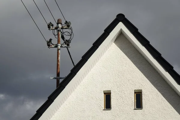 Een Elektriciteitspaal Een Dak Tegen Bewolkte Lucht — Stockfoto